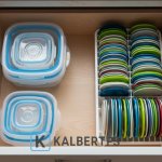 Laci dapur terorganisir: Tupperware disimpan bersarang (nesting) dan tutupnya tersusun vertikal di rak piring kecil. Tips penyimpanan cerdas KALBERTPS.